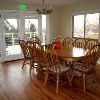 A cozy dining room with a wooden table and chairs, illuminated by natural light through large windows.