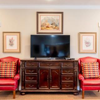 A stylish living room setup featuring a television on a wooden cabinet, flanked by red armchairs and framed artwork.