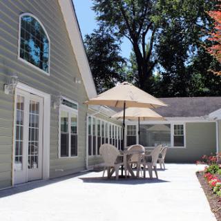 A bright and inviting outdoor patio area featuring a table with chairs and an umbrella, surrounded by lush trees.
