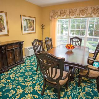 A cozy dining room with a large wooden table and chairs, adorned with a patterned carpet and natural light streaming in through a window.