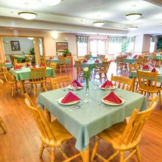 A bright and spacious dining area with neatly arranged tables and chairs, featuring green tablecloths and red napkins.