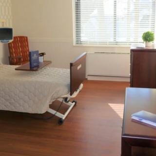 A hospital room with a single bed, bedside table, and a window allowing natural light in.