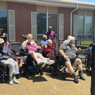 A group of elderly individuals sitting in wheelchairs outside on a sunny day.