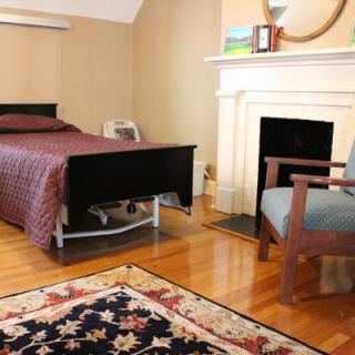 A cozy bedroom with a bed, chair, fireplace, and decorative rug.