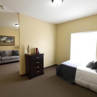 A view of a bedroom with a dresser, bed, and sofa in the adjoining room.