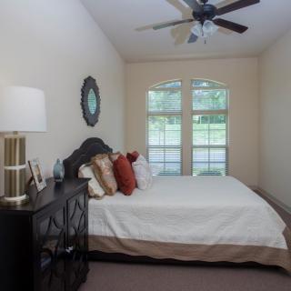 A neatly arranged bedroom with a bed, pillows, a lamp, and large windows.
