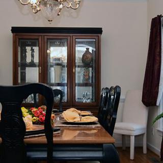 A cozy dining room with a wooden table set, surrounded by black chairs and complemented by a glass cabinet and chandelier.