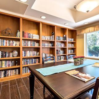 A cozy library room with wooden bookshelves filled with books and a table by the window.