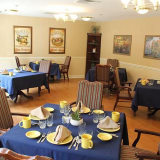 A cozy dining room with tables set for dining, featuring blue tablecloths and a warm interior decor.