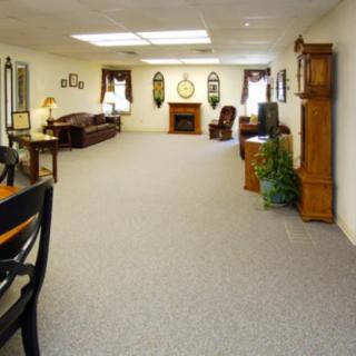 A spacious living room with classic furniture, featuring a sofa, chairs, a fireplace, and a grandfather clock.