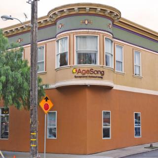 A corner building with distinctive architecture and a tree nearby, marked by a street sign.