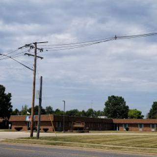 A view of a school building on a cloudy day, with electric poles and neatly trimmed grass in the foreground.