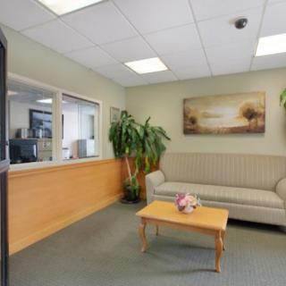 A cozy waiting room with a sofa, coffee table, and indoor plant, featuring a reception window and wall art.