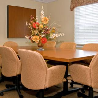 A conference room with a large table surrounded by chairs and a floral centerpiece.