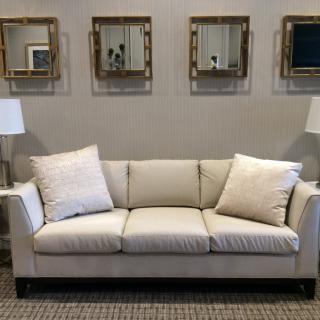 A stylish living room setup featuring a beige sofa with matching cushions, accompanied by two side lamps and decorative mirrors on the wall.