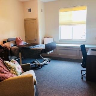 A room with a hospital bed, chair, and desk by the window.