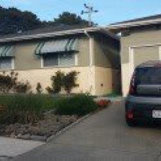 A suburban house with a car parked in the driveway and awnings over the windows.