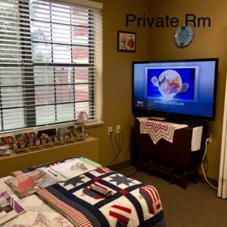 A cozy private bedroom featuring a quilted bed and a television under a window.