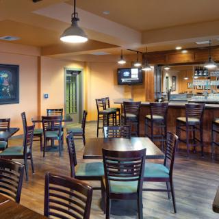 A well-lit dining area featuring tables and chairs, along with a bar setup in the background.