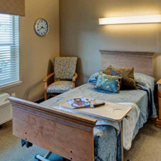 A hospital room with a bed, chair, and clock near a window.