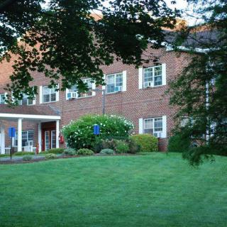 A brick building with white-trimmed windows surrounded by a neatly maintained lawn and trees.
