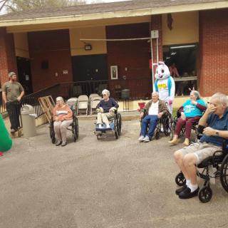 A group of elderly individuals in wheelchairs enjoying an outdoor activity with a person dressed in a costume.