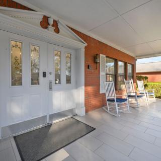 A welcoming porch with white double doors and rocking chairs against a brick wall.