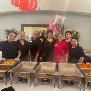 A group of catering staff smiling in front of a buffet setup at an event.