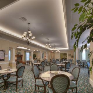 A well-decorated dining area with tables and chairs, illuminated by chandeliers, featuring carpeted flooring and greenery.
