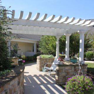 A charming outdoor patio featuring a white pergola, surrounded by lush greenery and landscaping.