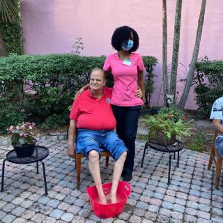 A person receives a foot bath while sitting outdoors on a patio with plants nearby.