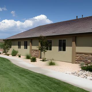 A modern building with a landscaped lawn and sidewalk under a blue sky with scattered clouds.