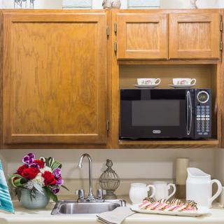 A cozy kitchen corner with a microwave, wooden cabinets, and a floral arrangement on the countertop.