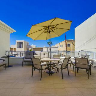 A sunny outdoor patio with a large umbrella, chairs, and tables in an urban setting.