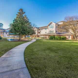 A scenic view of a residential building with a well-maintained lawn and surrounding trees.