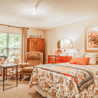 A cozy bedroom with vintage-style decor, featuring a quilted bed, armchair, and wooden furniture.