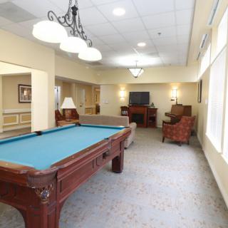 A well-lit recreation room featuring a pool table and comfortable seating with a television.