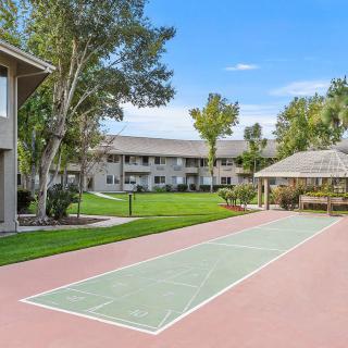A well-maintained apartment complex featuring a shuffleboard court, surrounded by green lawns and trees.