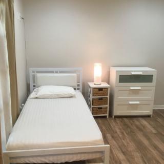 A minimalist bedroom with a single bed, a lamp on a nightstand, and a dresser.