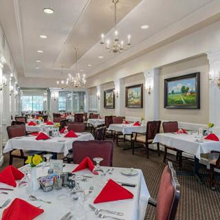 An elegant dining room with tables set with red napkins and chandeliers overhead.
