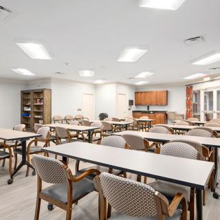 A bright and spacious conference room featuring multiple tables and chairs, with a small kitchen area in the background.