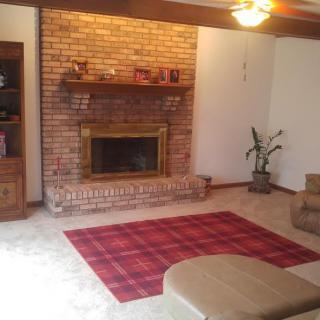 A cozy living room with a brick fireplace, a red plaid rug, and a ceiling fan.