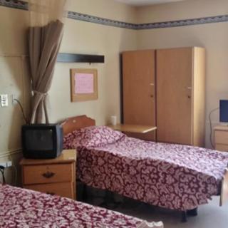 A hospital room with two twin beds, a wardrobe, and a small television.