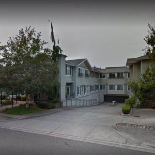 A multi-story residential building with a driveway and surrounding trees on an overcast day.