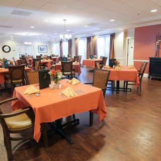 A spacious dining room featuring neatly set tables with orange tablecloths.
