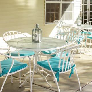 A sunlit patio with a white metal dining set featuring turquoise cushions and a decorative lantern on the table.