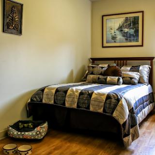 A cozy bedroom featuring a neatly made bed, decorative pillows, and a serene landscape painting.