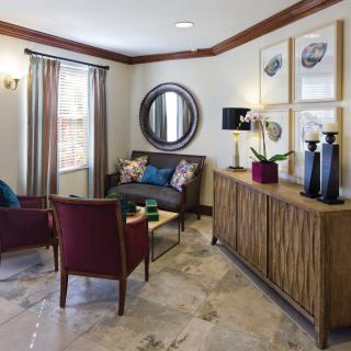A well-decorated living room featuring a sofa, two chairs, a round mirror, and a wooden cabinet with artistic decorations.