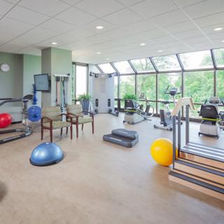 A well-lit gym with various exercise equipment and large windows.