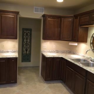 A well-lit kitchen featuring dark wood cabinets and a dual sink, with light countertops.
